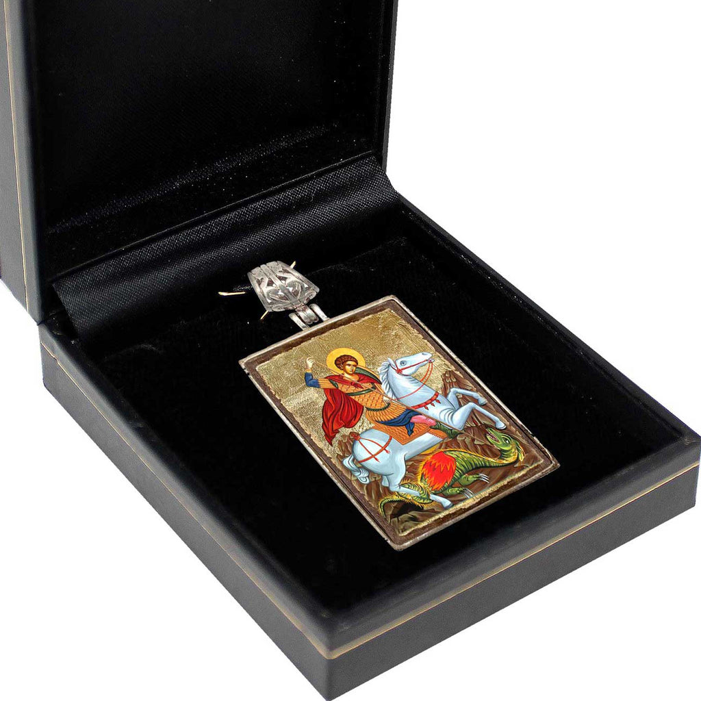 A black jewelry box containing a pendant with a religious icon, such as a saint or saintly figure, on a horse.