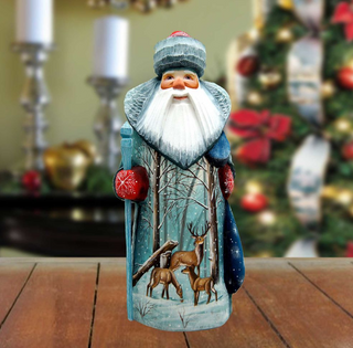 A wooden Santa Claus figurine with a white beard and hat, holding a blue staff and decorated with a winter scene of deer and snow.