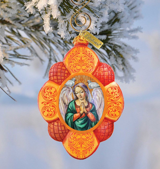 A decorative ornament featuring a painted image of an angel, hanging on a tree branch with snow on the branches.