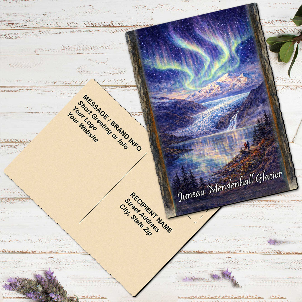 a postcard with a painting of a scenic mountain landscape, including a waterfall and a night sky with the aurora borealis. The postcard is placed on a white wooden surface, with some purple flowers nearby.