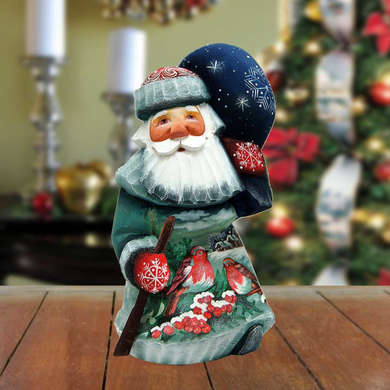 A wooden Santa Claus figurine holding a snowflake ornament and a bird ornament, set against a blurred background of Christmas decorations.