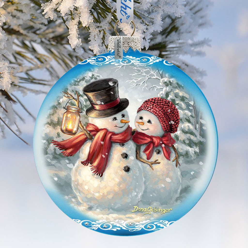 A blue ornament with a snowman and a lantern, hanging on a tree branch.