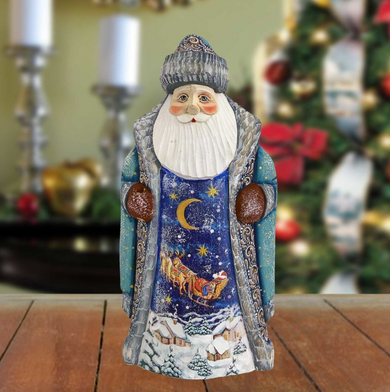 A figurine of Santa Claus wearing a blue and white outfit with a crescent moon and stars on the chest, standing on a wooden surface.