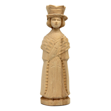A wooden sculpture of a woman wearing a hat and a long dress, standing upright and facing forward.