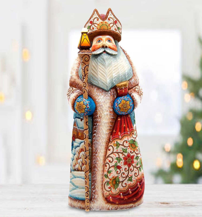A colorful, handcrafted wooden Santa Claus figurine stands on a wooden surface, wearing a red and gold hat and holding a lantern.