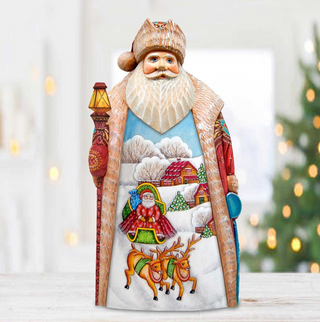 A wooden Santa Claus figurine with a detailed winter landscape design, including reindeer, houses, and trees, is displayed against a blurred background with Christmas lights.