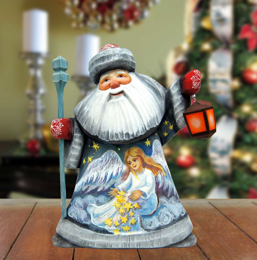 A wooden Santa Claus figurine holding a lantern and a star, with a painted angel on its chest, is displayed on a wooden surface.