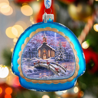 A blue ornament with a winter scene depicting a church, a bridge, and snow-covered trees.