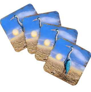 A set of four coasters featuring a blue heron standing on a beach against a backdrop of a sunset.