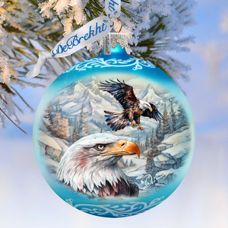 A blue Christmas ornament with a painting of two bald eagles in a snowy mountain landscape, hanging on a tree branch.
