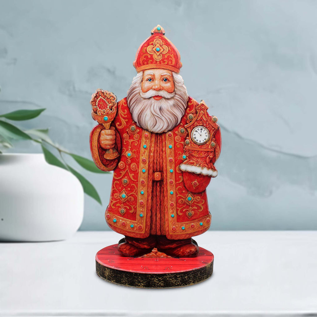 A figurine of Santa Claus wearing a red and gold robe and hat, holding a clock and a cup, standing on a red base.