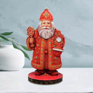 A figurine of Santa Claus wearing a red and gold robe and hat, holding a clock and a cup, standing on a red base.