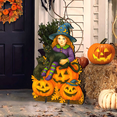 A Halloween-themed outdoor decoration featuring a young girl dressed as a witch, sitting on a pumpkin with a cat, and surrounded by jack-o-lanterns and hay bales.