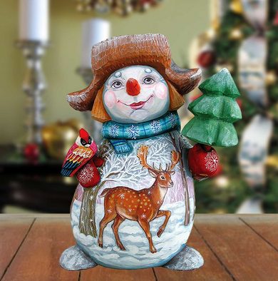 A hand-painted snowman figurine with a deer on its belly, holding a red bird, stands on a wooden surface.