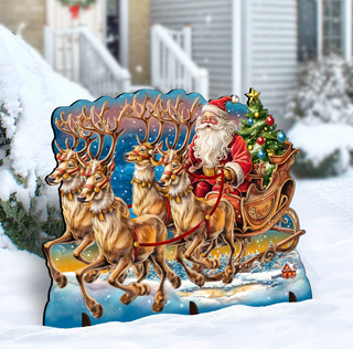 A cardboard cutout of Santa Claus riding a sleigh pulled by reindeer, with a Christmas tree and wreath in the background.