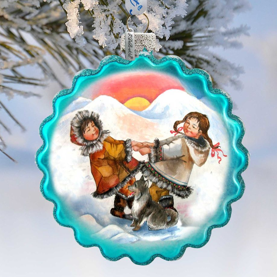 A decorative ornament featuring two children playing in the snow, with a dog in the background, against a snowy mountain landscape.