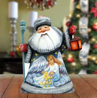 A wooden Santa Claus figurine holding a lantern and a star, with a painted angel on its chest, is displayed on a wooden surface.