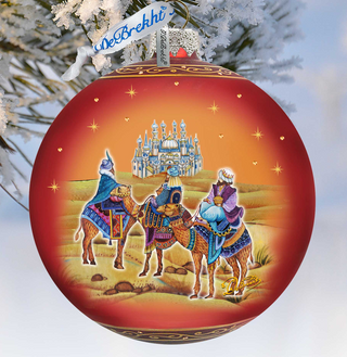 A red Christmas ornament with a painting of three wise men riding camels, set against a snowy landscape with a castle in the background.