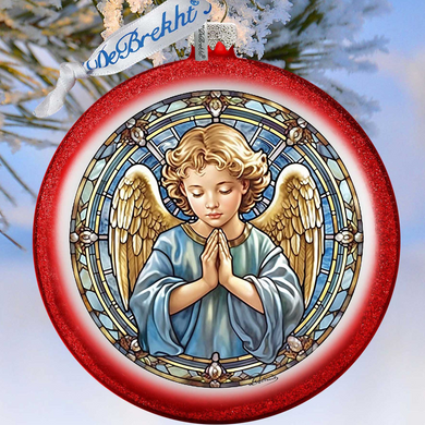 A red ornament with a stained glass design depicting a praying angel, hanging on a tree branch.