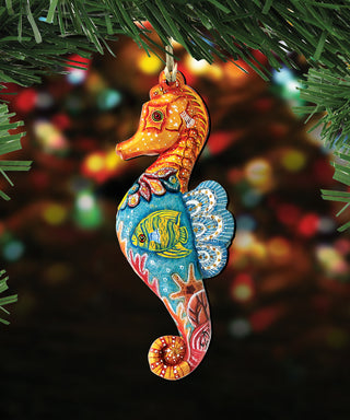 A colorful ornament in the shape of a seahorse, with a fish and other marine life designs, is hanging on a Christmas tree branch.