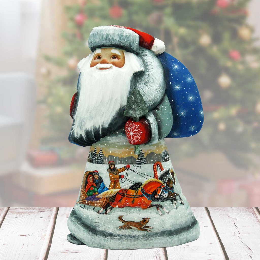 A hand-painted Santa Claus figurine with a blue bag and a sleigh, set against a blurred Christmas tree background.