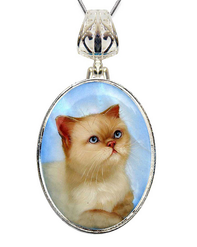 A silver pendant necklace with a round oval-shaped frame containing a close-up image of a cat with blue eyes and a pink nose.