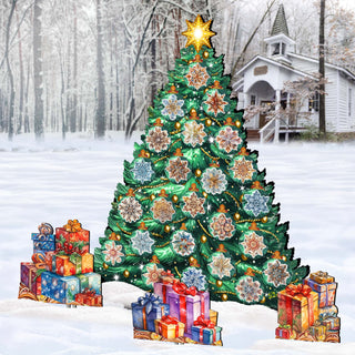 A large, brightly lit Christmas tree stands in a snowy landscape, surrounded by colorful presents and a white house in the background.
