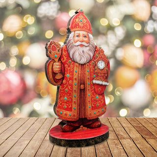 A wooden Santa Claus figurine holding a candelabra stands on a wooden surface against a blurred background of Christmas ornaments.