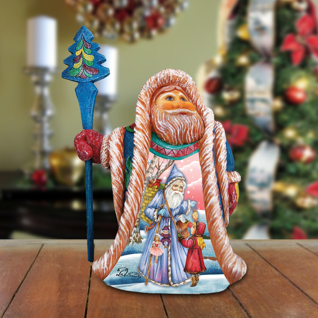 A figurine of Santa Claus holding a blue staff and a wreath, with a snowy landscape and other Christmas decorations in the background.