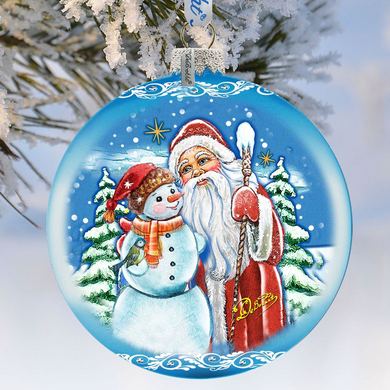 A blue ornament with a snowman and Santa Claus on a snowy background, hanging from a tree branch.