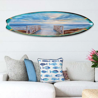 a large surfboard with a seascape painted on it, hanging on a wall above a white couch with colorful throw pillows.