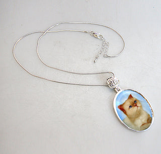 A silver necklace with a pendant featuring a picture of a cat.