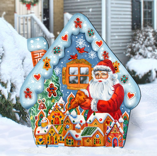 A large, colorful, and intricately decorated cardboard cutout of Santa Claus in a winter scene, with a snowy village and houses in the background.