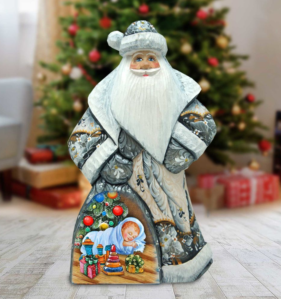A wooden Santa Claus figurine stands in front of a decorated Christmas tree, with a baby figure inside the Santa's pocket.