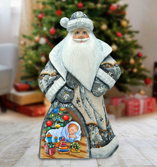 A wooden Santa Claus figurine stands in front of a decorated Christmas tree, with a baby figure inside the Santa's pocket.