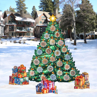 A large, colorful Christmas tree decorated with presents stands in the snow, surrounded by smaller wrapped gifts. In the background, there are houses and trees, creating a festive winter scene.
