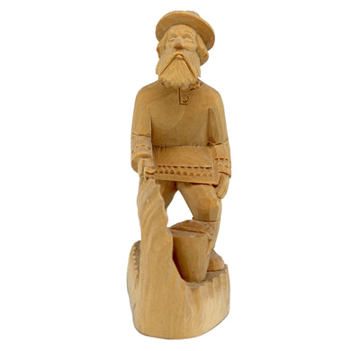 A wooden carving of a bearded man wearing a hat and holding a pipe, standing on a rock.