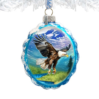 A glass ornament with a blue and white design depicting an eagle in flight against a mountainous landscape.