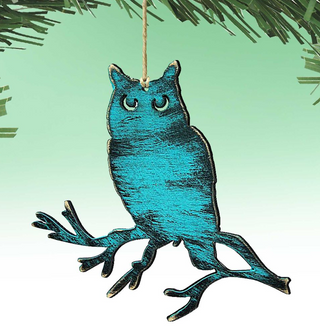 A blue owl ornament is hanging from a string against a green background.