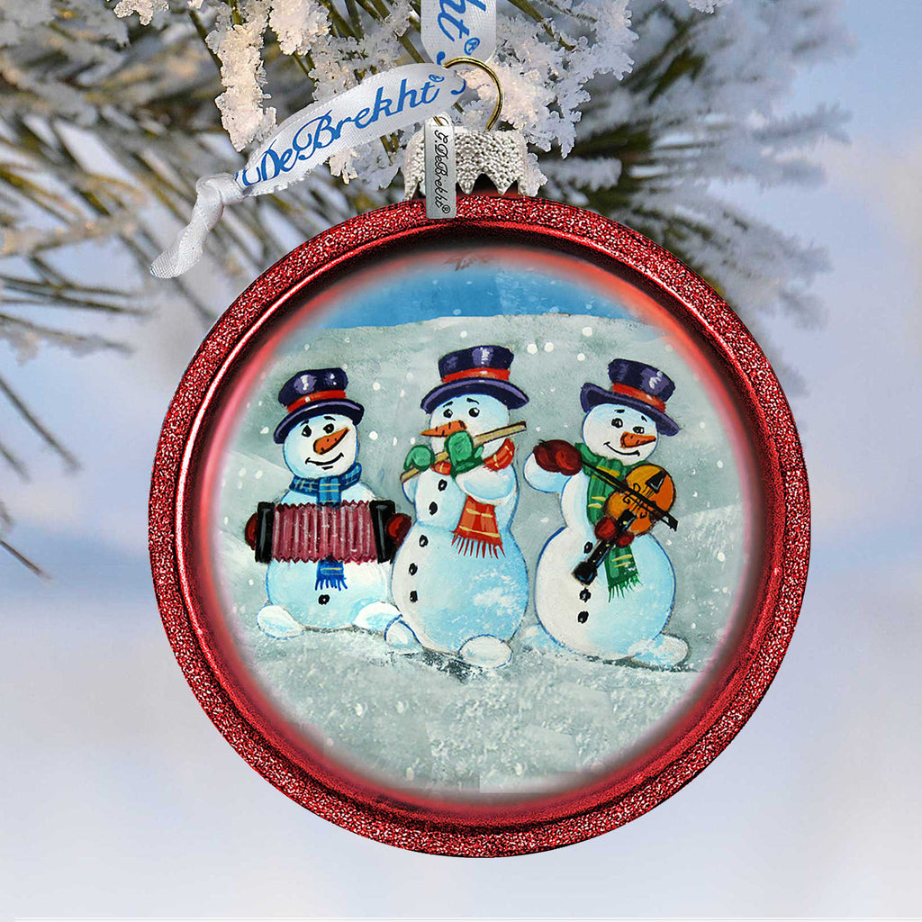 A red ornament with a snowy scene featuring three snowmen playing musical instruments.