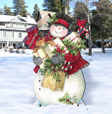 A snowman figure holding presents and a teddy bear stands in the snow, with a house and trees in the background.