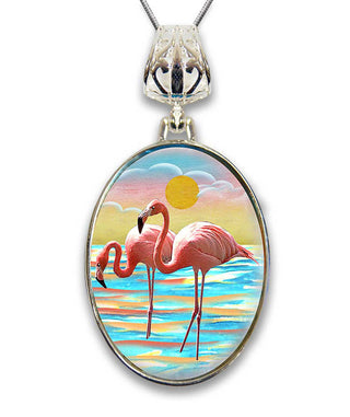 A pendant necklace with a circular design featuring two pink flamingos standing in a body of water, with a sunset in the background.