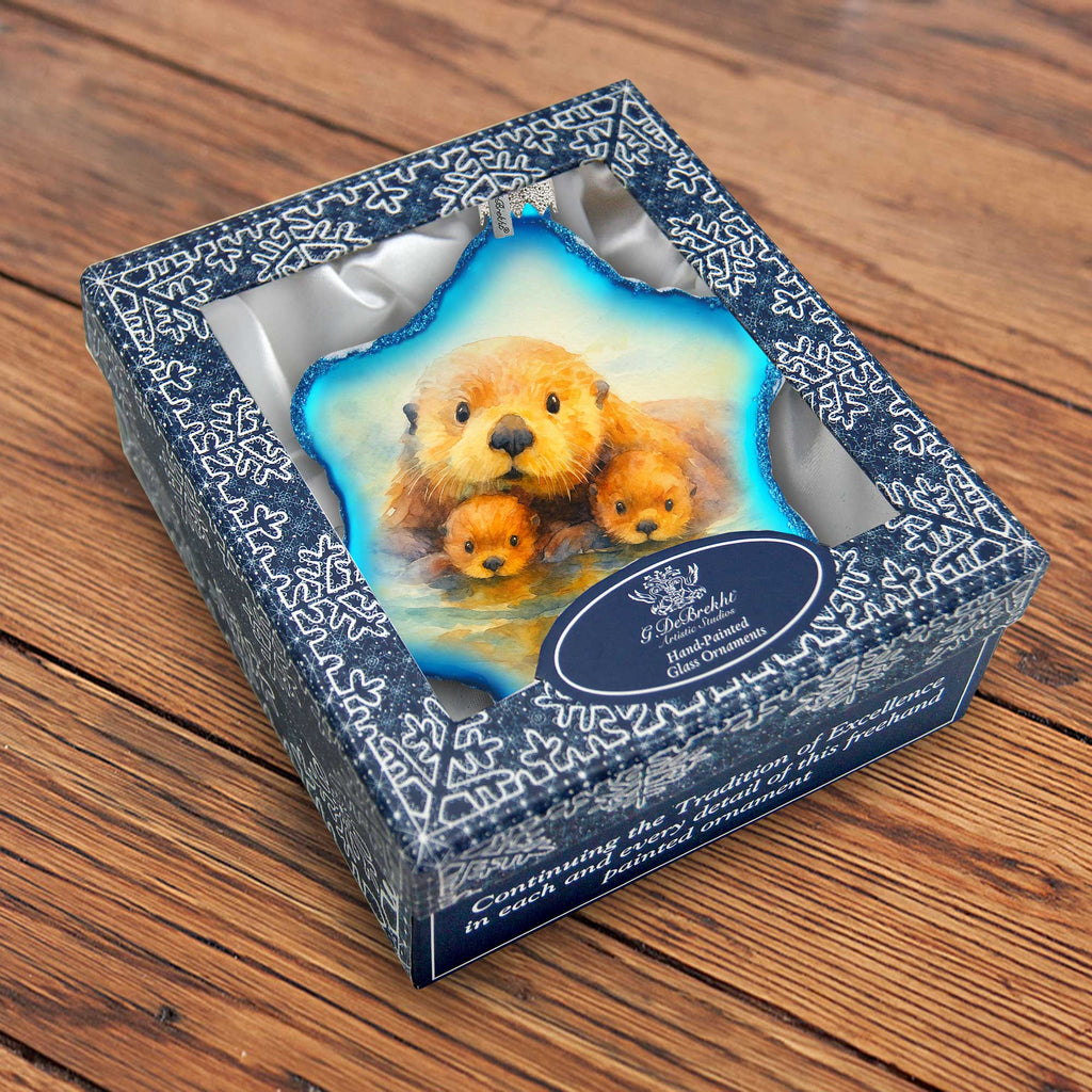 a decorative ornament in a blue and white box, depicting a family of otters.