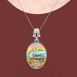 A necklace with a pendant featuring a colorful painting of a pelican on a beach.