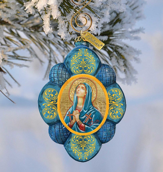 A blue and gold ornament featuring a depiction of a woman in a blue robe and holding a cross, hanging from a tree branch.