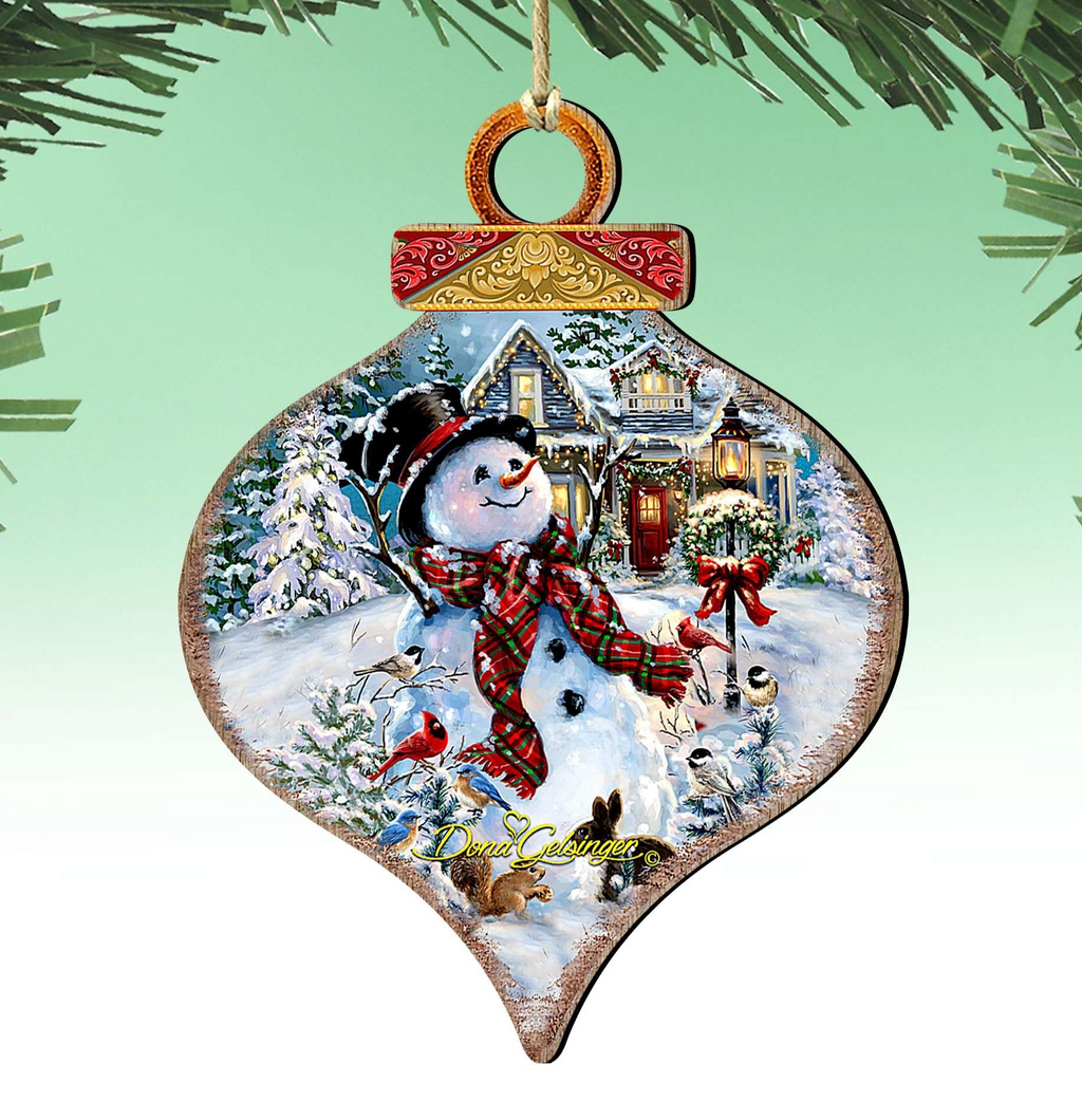 A snowman ornament with a wreath and a bird perched on its arm, set against a snowy winter landscape with a house and trees.