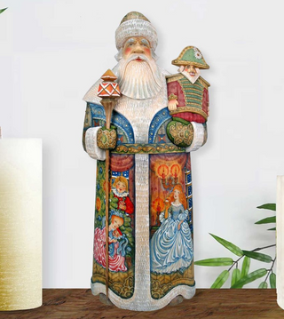 A colorful and intricately carved wooden Santa Claus figure, adorned with various scenes and figures, stands on a wooden surface.