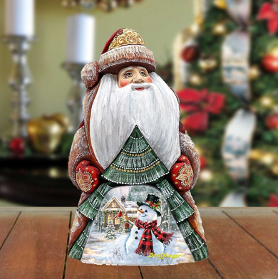 A wooden Santa Claus figurine with a white beard and hat, standing on a wooden surface. The figurine has a snowman and Christmas tree depicted on its chest.