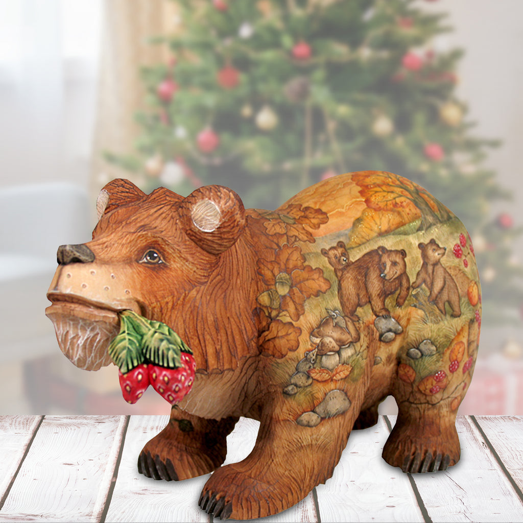 A wooden bear figurine with a painted design of bears and berries, placed on a wooden surface in front of a blurred Christmas tree.