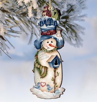 A snowman ornament with a birdhouse, a hat, and a scarf, hanging from a tree branch against a snowy background.